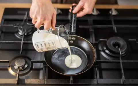 Mani versano panna da cucina in una padella su un fornello a gas.