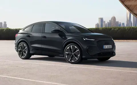 Elegancki, czarny Audi Q4 e-tron, elektryk z dynamiczną linią nadwozia, zaparkowany na tle nowoczesnej panoramy miasta.