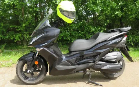 Czarny skuter Kawasaki J300 z jaskrawożółtym kaskiem zawieszonym na kierownicy, gotowy do jazdy w słoneczny dzień.