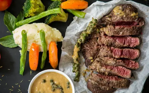 Succulenta costata di manzo affettata, servita con purè, verdure miste e salsa al pepe verde.
