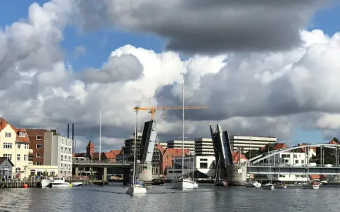 Sonderborg Hafen mit geöffneter Klappbrücke, Segelbooten und Gebäuden unter dramatischem Wolkenhimmel.