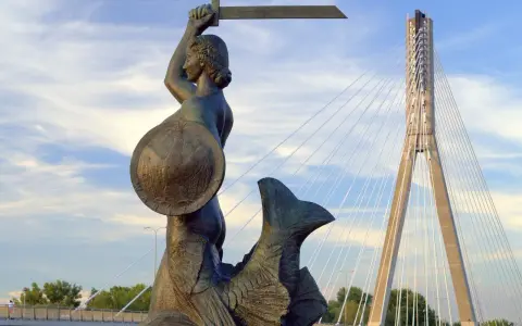 Syrenka Warszawska z mieczem i tarczą, symbol legendy o syrence warszawskiej, na tle nowoczesnego mostu.