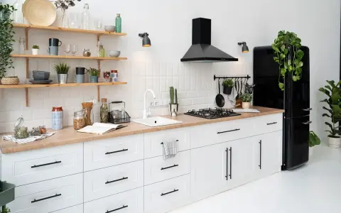 Cocina moderna con gabinetes blancos y encimera de madera. El diseño para pintar cocinas es minimalista, con electrodomésticos negros y estantes de madera.
