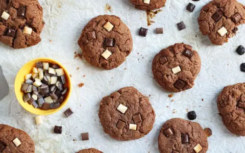 Gros plan sur des cookies au chocolat parsemés de morceaux de chocolat blanc et noir. Un petit bol jaune contient des morceaux de chocolat, comme un cookie stick.