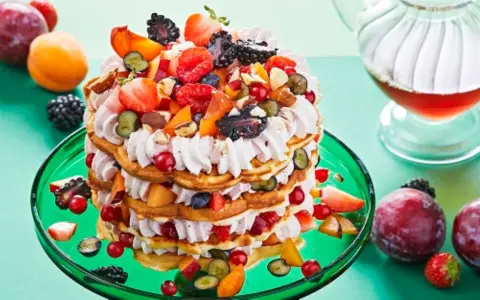 Eine beeindruckende Waffeltorte mit Erdbeeren und Mascarpone, geschichtet mit frischen Beeren und Früchten, auf einem grünen Teller.