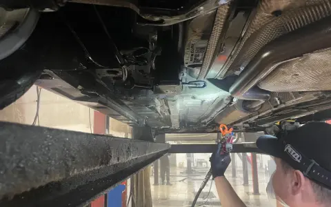 Profesjonalne zabezpieczenie antykorozyjne podwozia samochodu. Mechanik aplikuje preparat ochronny.