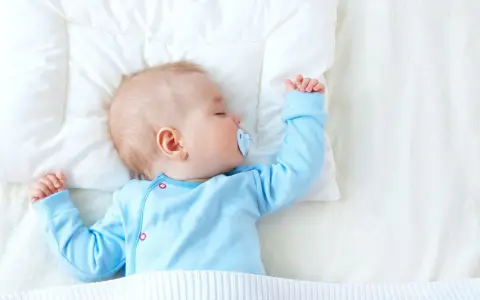 Śpiące dziecko w niebieskim pajacyku, z smoczkiem. Delikatna asymetria ułożeniowa może być korygowana ćwiczeniami w domu.