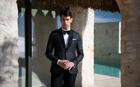 Elegancki mężczyzna w smokingu, idealny przykład stroju black tie na wesele. Różnica między ubiorem black tie a cocktail dress dla gości weselnych jest widoczna.