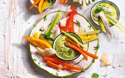 Deliziosi antipasti vegetariani: bastoncini di carote, peperoni e sedano con salsa verde cremosa, guarniti con scaglie di formaggio e menta.