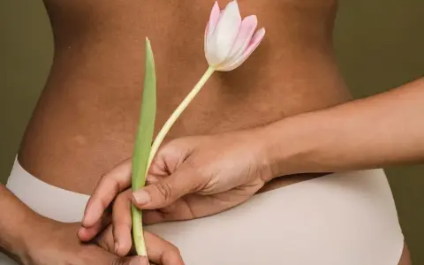 Delikatne rozstępy na plecach, ukryte za tulipanem. Ciało w beżowej bieliźnie.