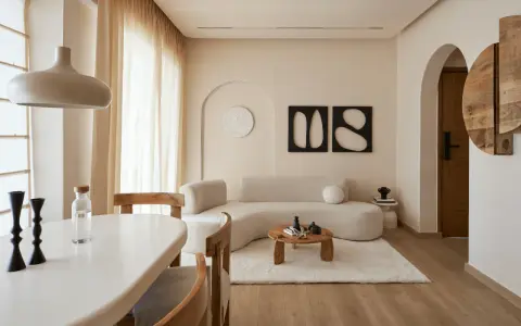 Un soggiorno in stile wabi sabi con divano curvo, tavolino in legno grezzo, tappeto soffice e decorazioni minimaliste.