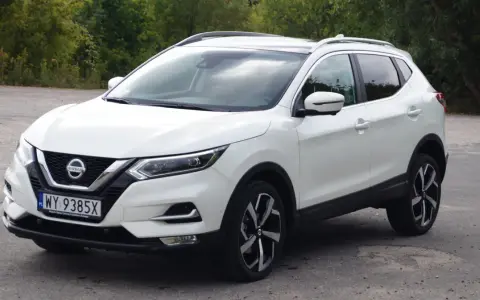 Biały Nissan Qashqai 2014 z polskimi tablicami rejestracyjnymi stoi na drodze, otoczony zielenią drzew.