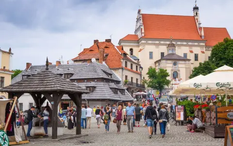 Tłum ludzi spaceruje po brukowanym rynku, podziwiając zabytkową architekturę. To urokliwe turystyczne miasta w Polsce.