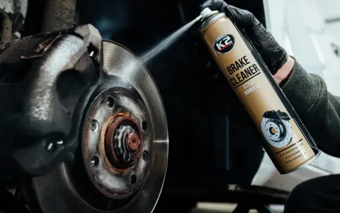 Ręka w czarnej rękawiczce rozpyla środek na zużyte tarcze hamulcowe. Preparat K2 Brake Cleaner skutecznie czyści hamulce.