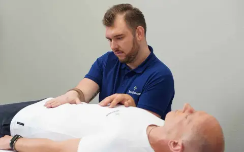 Terapeuta wykonuje zabieg z zakresu osteopatii wisceralnej, delikatnie dotykając brzucha pacjenta.