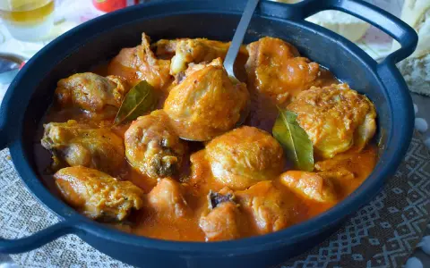 Sabroso pollo a la cerveza en cazuela negra, con salsa naranja y hojas de laurel.