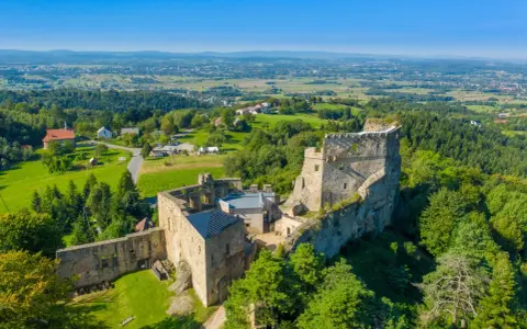 Ruiny zamku na wzgórzu, otoczone zielenią, w oddali widać miasto. To malowniczy rezerwat prządki.
