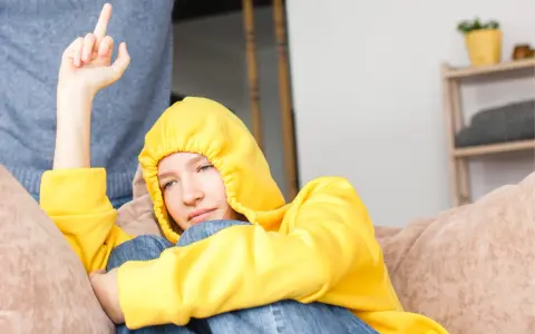 Ein Teenager in gelbem Hoodie zeigt seiner Mutter den Mittelfinger. Er hat keinen Respekt vor ihr.