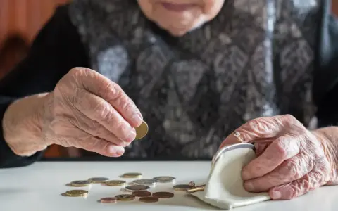 Dłoń starszej osoby liczy monety, zastanawiając się, kiedy najlepiej przejść na emeryturę w 2026 roku.