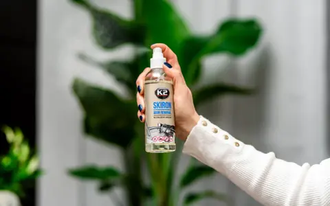 Dłoń trzyma butelkę K2 SKIRON ODOR REMOVAL, która rozpyla mgiełkę, by zlikwidować nieprzyjemny zapach w pokoju po nocy.