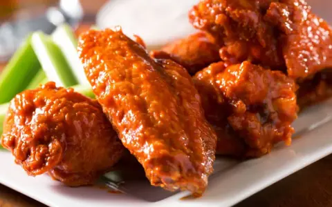 Alitas de pollo en freidora de aire, cubiertas de salsa picante, servidas con bastones de apio crujientes. ¡Un aperitivo irresistible!
