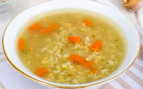 Aromaticzna zupa na rosole z makaronem i marchewką, podana w białej miseczce ze złotym rantem.