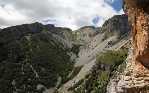 Un sentiero serpeggia tra montagne rocciose e vegetazione rigogliosa, un'avventura estiva al passo lanciano.
