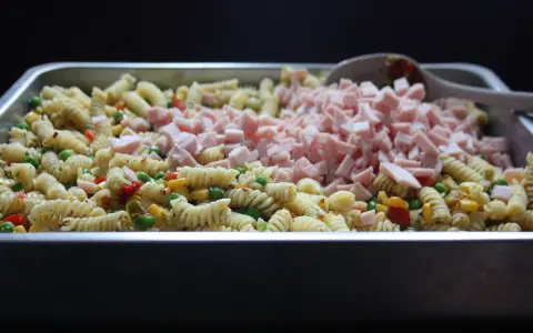 Stor ugnsform fylld med pastasallad med kassler, grönsaker och en sked.