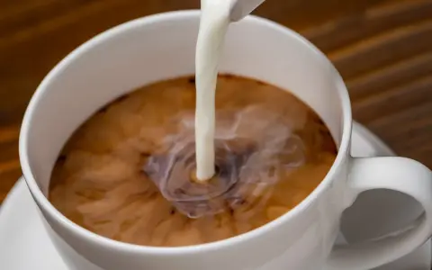 Biała filiżanka kawy, do której wlewane jest mleko. Zastanawiasz się nad mleko owsiane kcal?