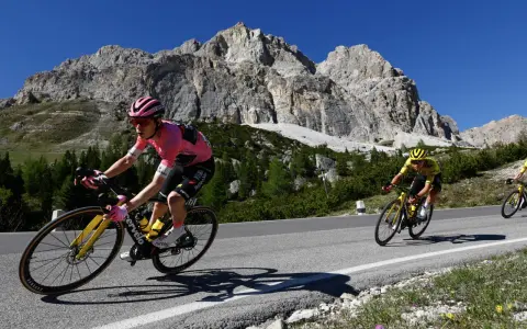 Cyclist in pink jersey, likely the winner of the Giro d'Italia, climbs a mountain road with a dramatic rocky peak behind.