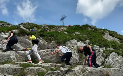 Grupa turystów wspina się po kamienistym zboczu, pokonując najtrudniejszy szlak na Giewont. W tle widoczny krzyż.