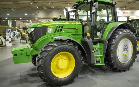Zielony traktor marki John Deere 6155 M, gotowy do pracy na polu.