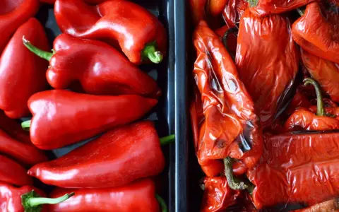 Dos recipientes llenos de pimientos rojos. A la izquierda, pimientos frescos y brillantes. A la derecha, pimientos asados, con la piel arrugada y un tono más oscuro.