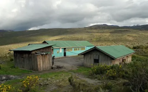 Proste chatki z zielonymi dachami na tle surowego krajobrazu u podnóża góry Mt Kenya.