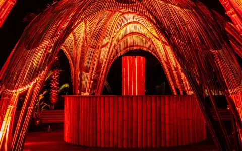 Struttura in bambù illuminata di rosso, con un bancone e un'installazione luminosa centrale. Atmosfera da house techno.