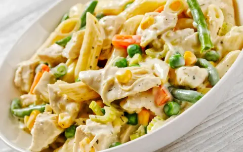 Penne z kurczakiem i warzywami w kremowym sosie. Danie zawiera zieloną fasolkę, groszek, kukurydzę i marchewkę.