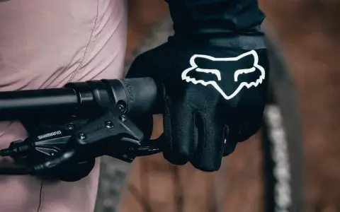 Dłoń w czarnej rękawiczce Fox z białym logo, gotowa do jazdy. Idealne rękawiczki na rower dla każdego miłośnika dwóch kółek.