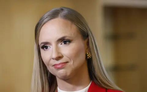 Sara Skyttedal, med sitt blonda hår och röda kavaj, ler snett mot kameran.