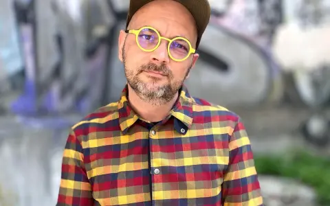 Filip Springer w okularach i koszuli w kratę, na tle graffiti.