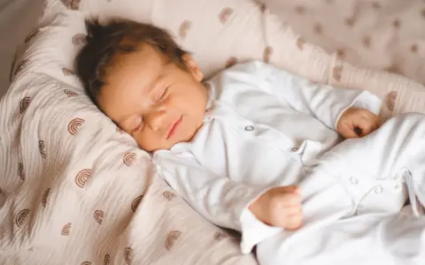 Un neonato dorme sereno, avvolto in una copertina con arcobaleni. Un dolce sogno per questi bambini piccoli.