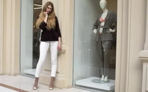 Modelka w białych spodniach i bordowej marynarce obok manekina w eleganckim stroju. Skandynawskie marki odzieżowe prezentują najnowsze trendy.
