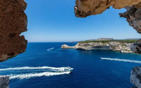 Blick durch Felsformationen auf das tiefblaue Meer bei Bonifacio, Korsika. Boote gleiten über die Wellen.