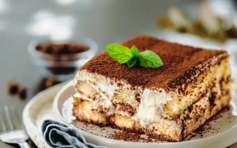 Un délicieux tiramisu anniversaire, saupoudré de cacao et garni d'une feuille de menthe fraîche, prêt à être dégusté.