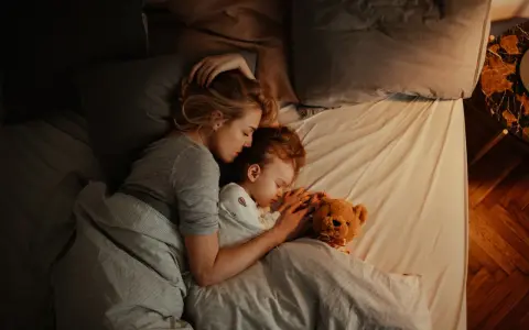 Mutter und Kind schlafen eng umschlungen. Ab wann Babys bewusst kuscheln, zeigt diese Szene der Geborgenheit.