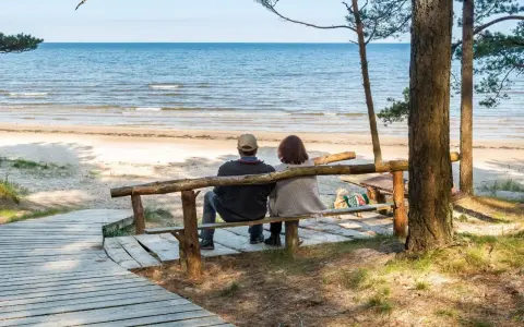 Para relaksująca para siedzi na ławce, patrząc na morze. Idealne miejsce na sanatoria nad morzem.