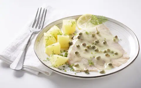 Une aile de raie nappée d'une sauce crémeuse aux câpres, accompagnée de pommes de terre et d'une tranche de citron.