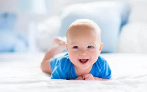 Uśmiechnięty bobas na brzuchu, ćwiczący podnoszenie głowy. To jeden z kluczowych etapów rozwoju ruchowego dziecka.