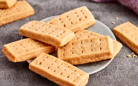 Goldbraune Shortbread-Kekse, perfekt für ein einfaches Shortbread Rezept. Sie liegen auf einem Teller und daneben ein lila Tuch.