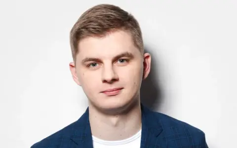 Młody mężczyzna w niebieskiej marynarce w kratę, gotowy do występu. Polski stand up w jego wykonaniu to gwarancja dobrej zabawy.