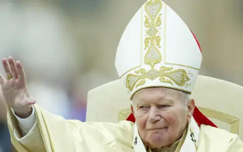 Papież Jan Paweł II w białej mitrze z haftem, pozdrawia wiernych. Jego dłoń z pierścieniem jest uniesiona. Codzienna modlitwa do św. Jana Pawła II.